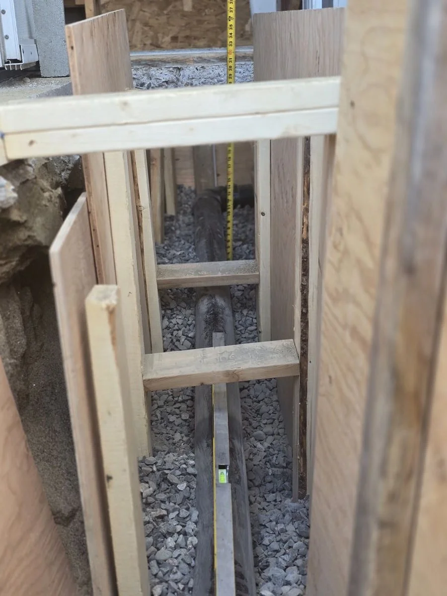New underground drain line bedded in gravel inside a shored trench