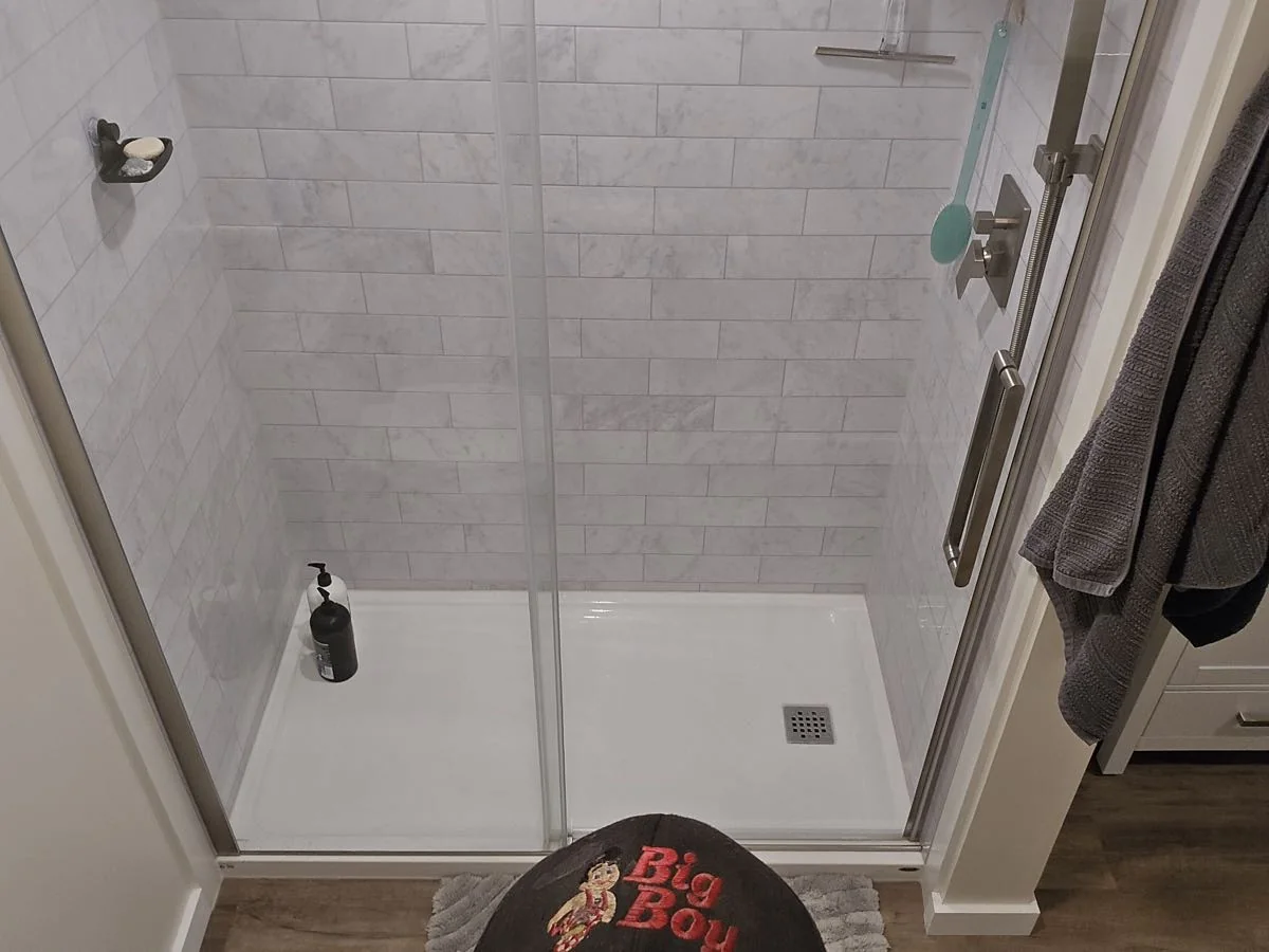 Marble subway tile shower with sliding glass doors and a Big Boy Enterprises mat