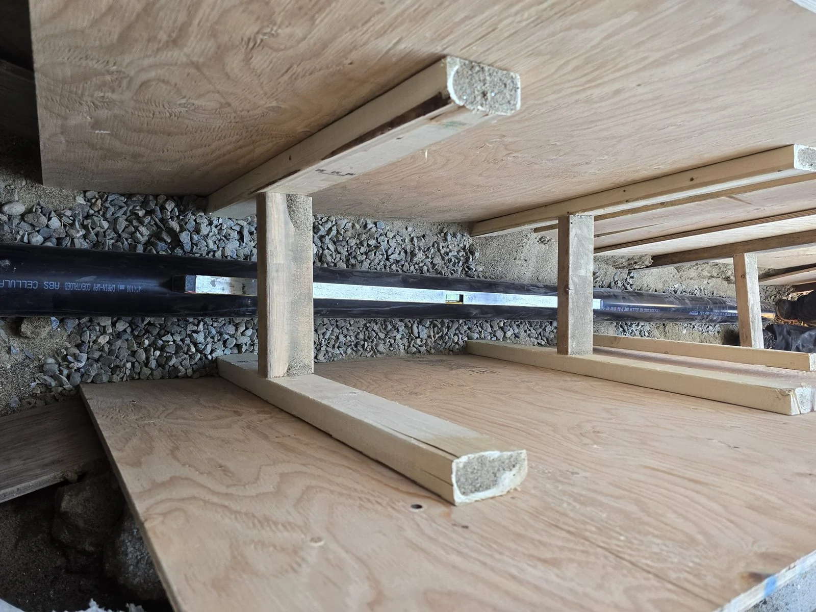New underground drain line bedded in gravel inside a shored trench